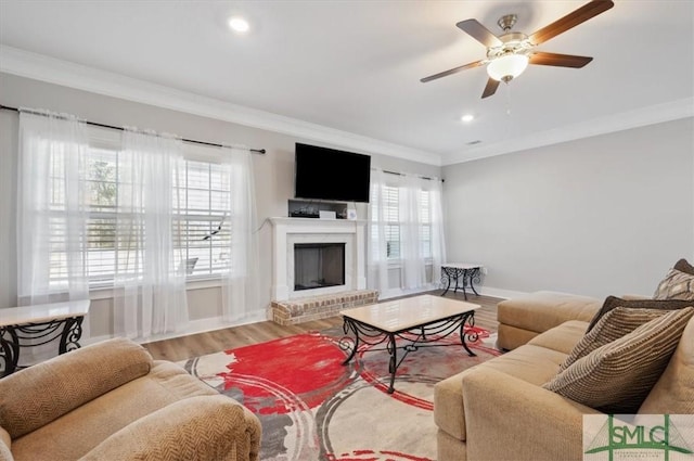 living room with a fireplace, wood-type flooring, ornamental molding, and ceiling fan