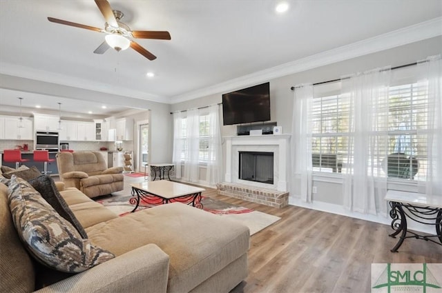 living room with ornamental molding, ceiling fan, a fireplace, and light hardwood / wood-style floors