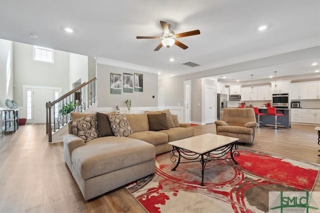 living room featuring ceiling fan, ornamental molding, and light wood-type flooring