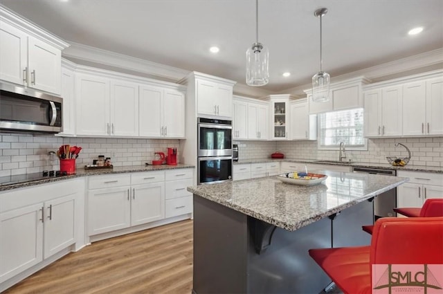 kitchen featuring white cabinetry, appliances with stainless steel finishes, a kitchen breakfast bar, and decorative light fixtures