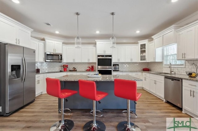 kitchen with stainless steel appliances, decorative light fixtures, a center island, and light stone countertops