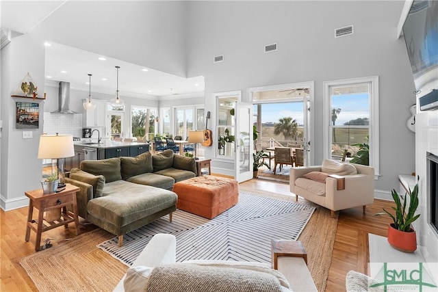 living room featuring sink, a towering ceiling, ornamental molding, and light hardwood / wood-style floors