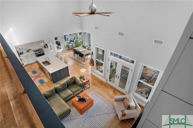 living room featuring hardwood / wood-style floors, sink, a high ceiling, ceiling fan, and french doors