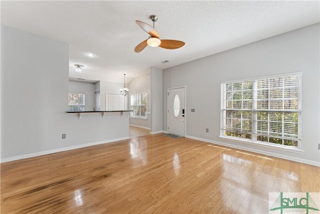 unfurnished living room with ceiling fan with notable chandelier, light hardwood / wood-style flooring, and a textured ceiling