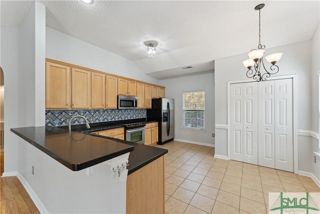 kitchen with lofted ceiling, decorative light fixtures, kitchen peninsula, stainless steel appliances, and backsplash