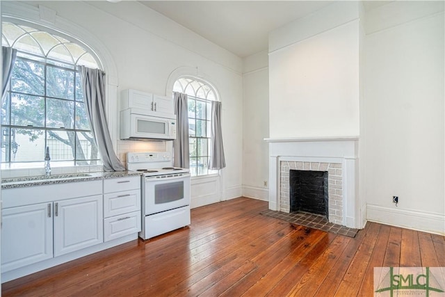 kitchen with a fireplace, white cabinetry, sink, dark wood-type flooring, and white appliances