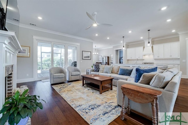 living room featuring sink, a brick fireplace, ornamental molding, dark hardwood / wood-style floors, and ceiling fan with notable chandelier