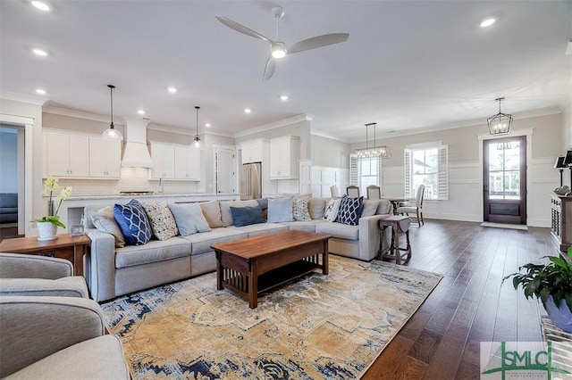 living room featuring dark wood-type flooring, crown molding, and ceiling fan with notable chandelier