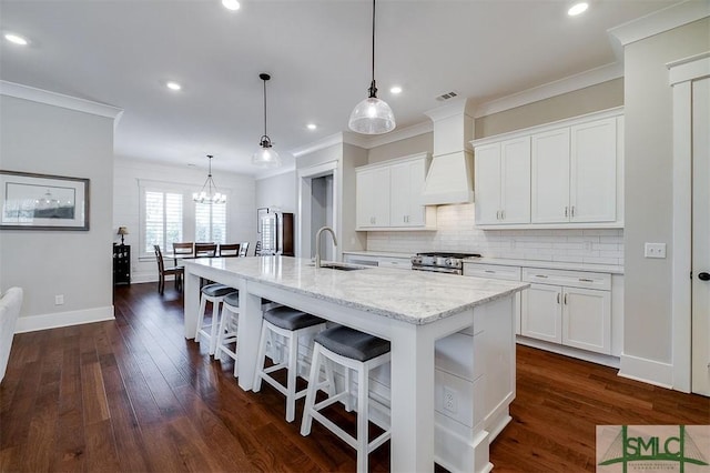 kitchen featuring custom range hood, decorative light fixtures, an island with sink, and white cabinets