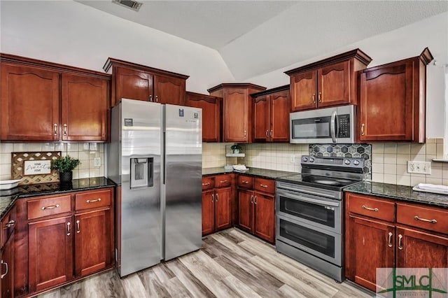 kitchen featuring stainless steel appliances, light hardwood / wood-style floors, decorative backsplash, vaulted ceiling, and dark stone counters