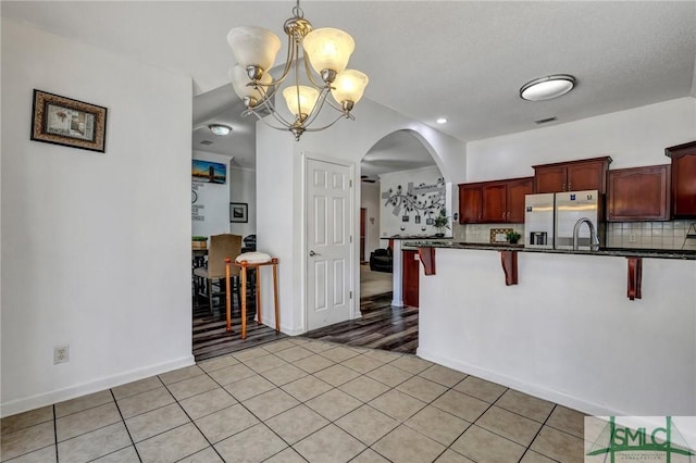 kitchen with light tile patterned flooring, a kitchen bar, tasteful backsplash, decorative light fixtures, and stainless steel fridge