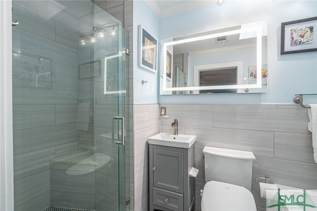 bathroom featuring toilet, a shower with shower door, crown molding, tile walls, and vanity