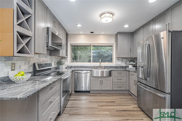 kitchen featuring gray cabinets, appliances with stainless steel finishes, sink, dark stone countertops, and light hardwood / wood-style flooring