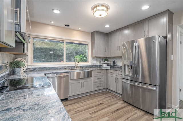 kitchen featuring appliances with stainless steel finishes, sink, light hardwood / wood-style flooring, and dark stone counters