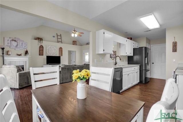 dining room featuring dark wood-type flooring, sink, vaulted ceiling, ceiling fan, and a fireplace