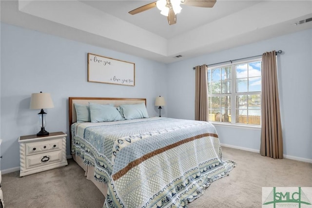 bedroom with light carpet, a tray ceiling, and ceiling fan