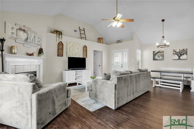 living room featuring high vaulted ceiling, dark hardwood / wood-style flooring, a tiled fireplace, and ceiling fan with notable chandelier