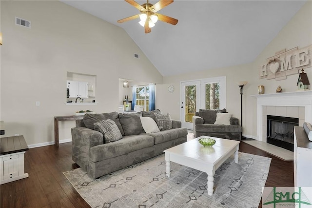 living room with a tile fireplace, dark wood-type flooring, ceiling fan, and high vaulted ceiling