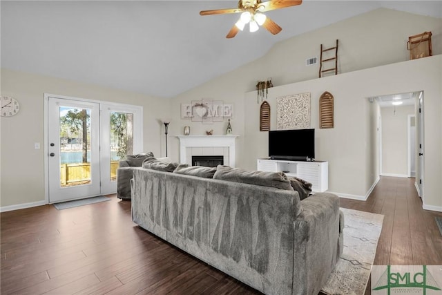 living room featuring dark wood-type flooring, ceiling fan, a tiled fireplace, and vaulted ceiling