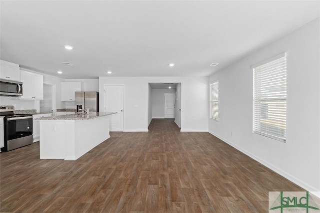 kitchen featuring appliances with stainless steel finishes, white cabinetry, a kitchen island with sink, light stone counters, and dark wood-type flooring