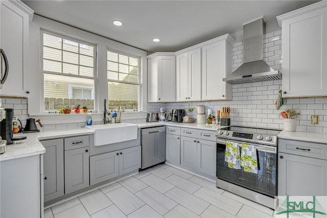 kitchen with wall chimney exhaust hood, sink, appliances with stainless steel finishes, gray cabinets, and backsplash