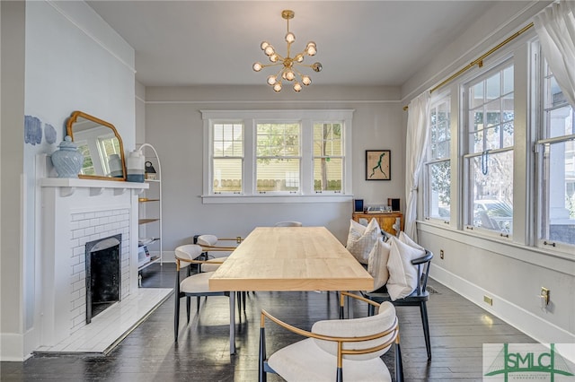 dining room featuring a brick fireplace, dark wood-type flooring, plenty of natural light, and a chandelier