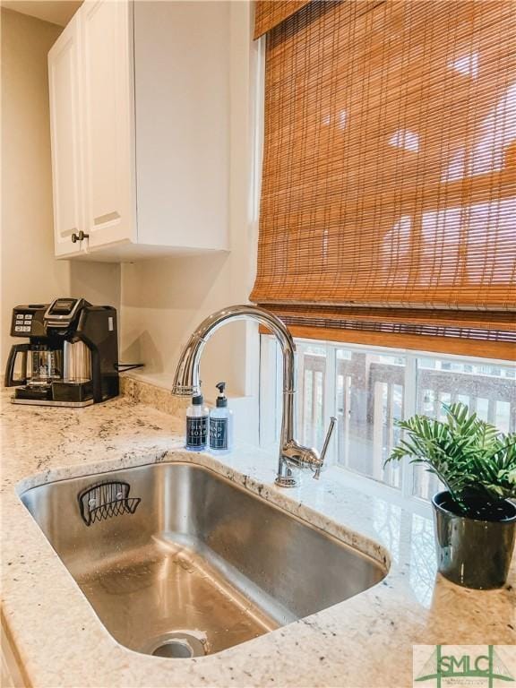 interior details featuring white cabinetry, sink, and light stone counters