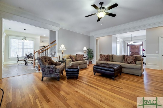 living room with ornamental molding, ceiling fan with notable chandelier, and light wood-type flooring