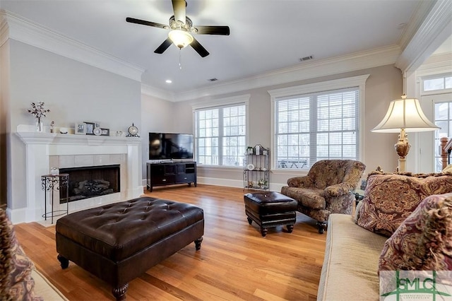 living room featuring ceiling fan, ornamental molding, wood-type flooring, and a tile fireplace