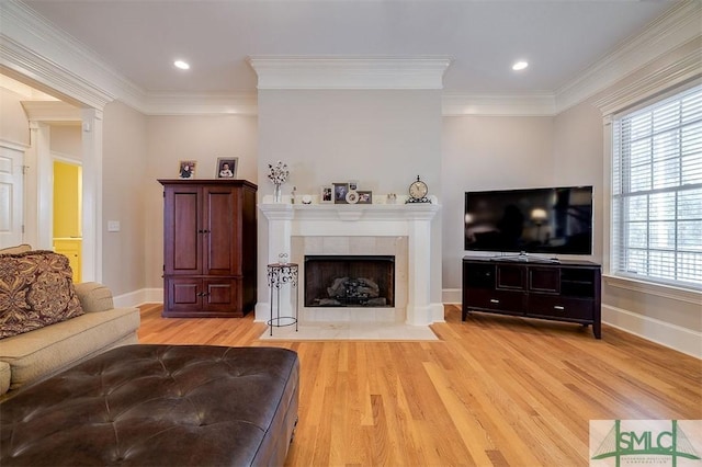 living room featuring a tiled fireplace, ornamental molding, and light wood-type flooring