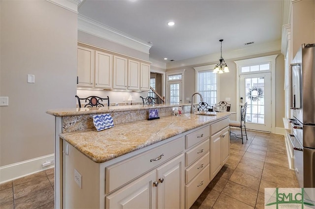 kitchen with sink, stainless steel fridge, a kitchen island with sink, light stone countertops, and decorative light fixtures