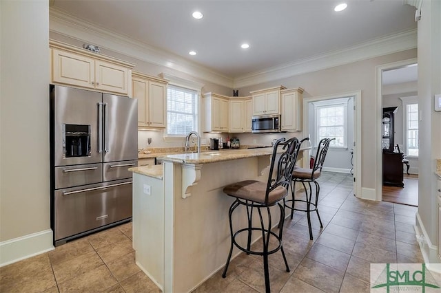 kitchen featuring a breakfast bar, stainless steel appliances, light stone countertops, and cream cabinets