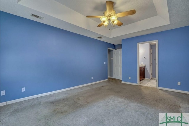 unfurnished bedroom featuring light carpet, a tray ceiling, ceiling fan, and ensuite bathroom