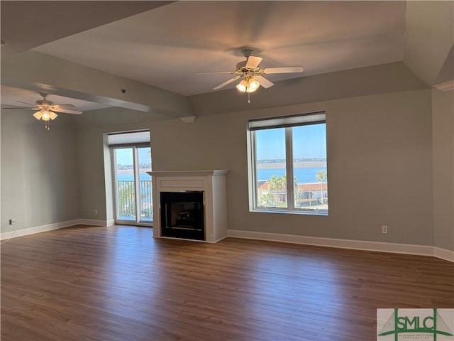 unfurnished living room with dark hardwood / wood-style flooring, a wealth of natural light, ceiling fan, and a water view