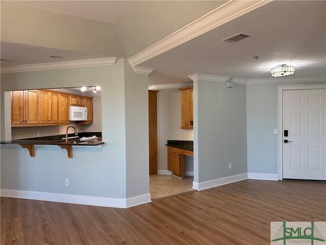 kitchen featuring hardwood / wood-style floors, crown molding, built in desk, and a kitchen bar