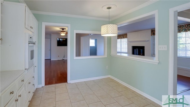 unfurnished dining area with light tile patterned floors, a wealth of natural light, ornamental molding, and ceiling fan