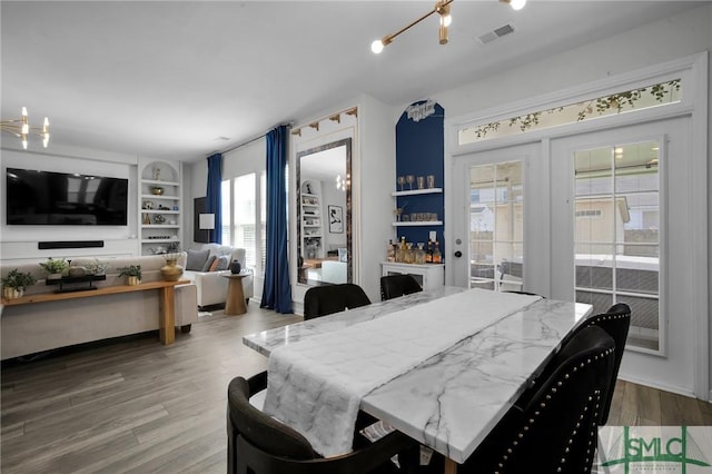 dining space with wood-type flooring, built in features, and an inviting chandelier