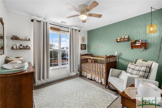 carpeted bedroom with a crib and ceiling fan