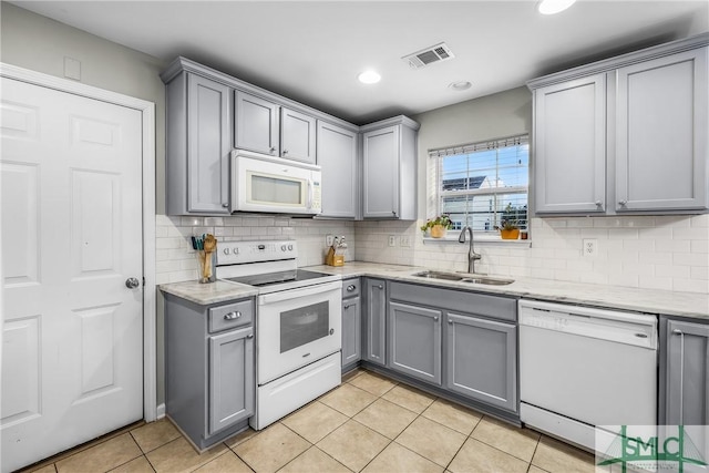 kitchen featuring sink, white appliances, gray cabinets, light tile patterned floors, and tasteful backsplash