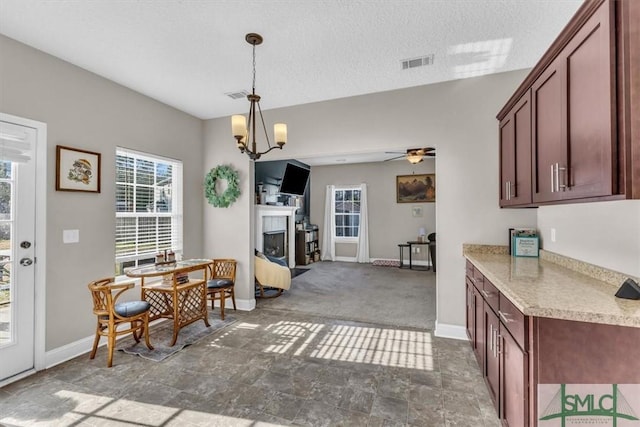 kitchen featuring hanging light fixtures, dark carpet, ceiling fan with notable chandelier, and a textured ceiling