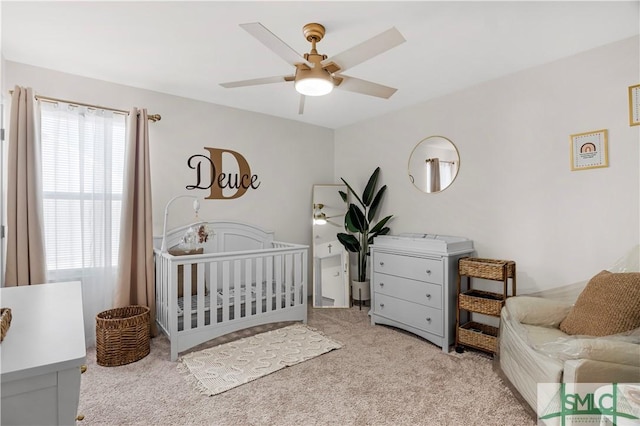 carpeted bedroom featuring a nursery area and ceiling fan