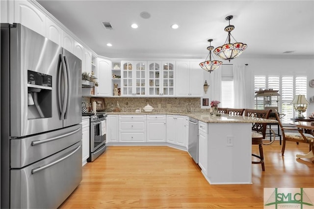 kitchen featuring decorative light fixtures, appliances with stainless steel finishes, kitchen peninsula, light stone countertops, and white cabinets