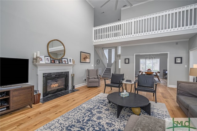 living room featuring wood-type flooring, a high ceiling, ornamental molding, a high end fireplace, and an inviting chandelier