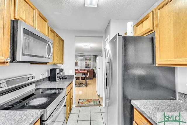 kitchen with stainless steel appliances, ceiling fan, light tile patterned floors, and a textured ceiling