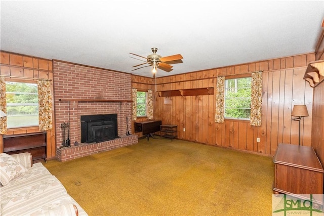 carpeted living room featuring a brick fireplace, plenty of natural light, ceiling fan, and wood walls