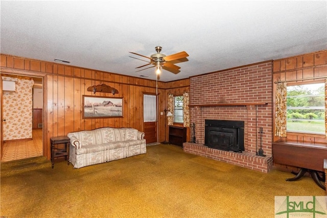 carpeted living room featuring a brick fireplace, wooden walls, a textured ceiling, and ceiling fan