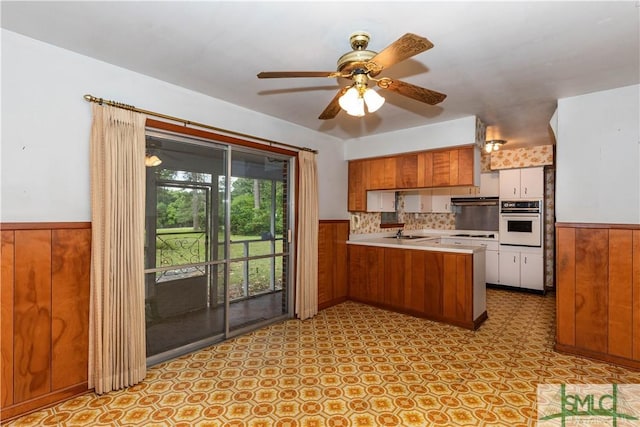 kitchen featuring sink, wooden walls, kitchen peninsula, and white oven