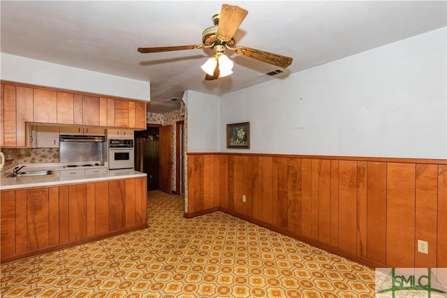 kitchen with wood walls, sink, ceiling fan, cooktop, and white oven