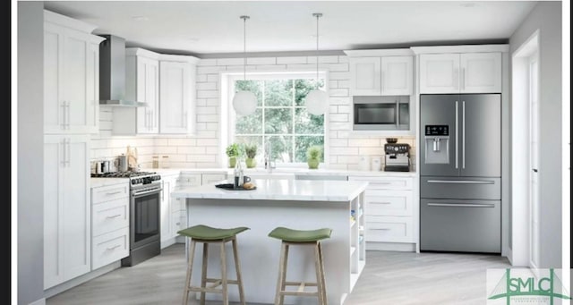 kitchen featuring pendant lighting, white cabinetry, a center island, stainless steel appliances, and wall chimney range hood