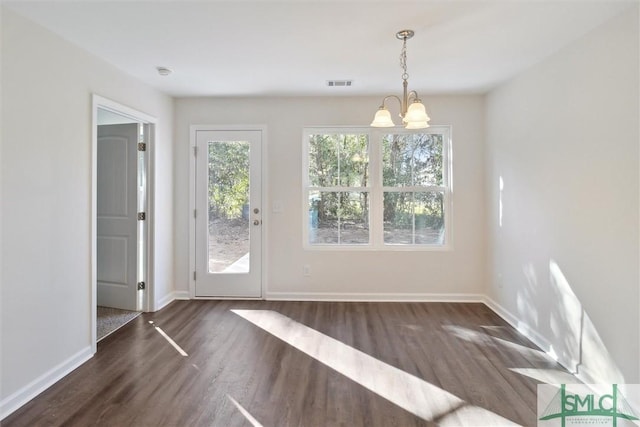 unfurnished dining area featuring dark wood-type flooring, a healthy amount of sunlight, and an inviting chandelier